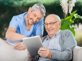 Happy Caretaker And Senior Man Using Tablet PC