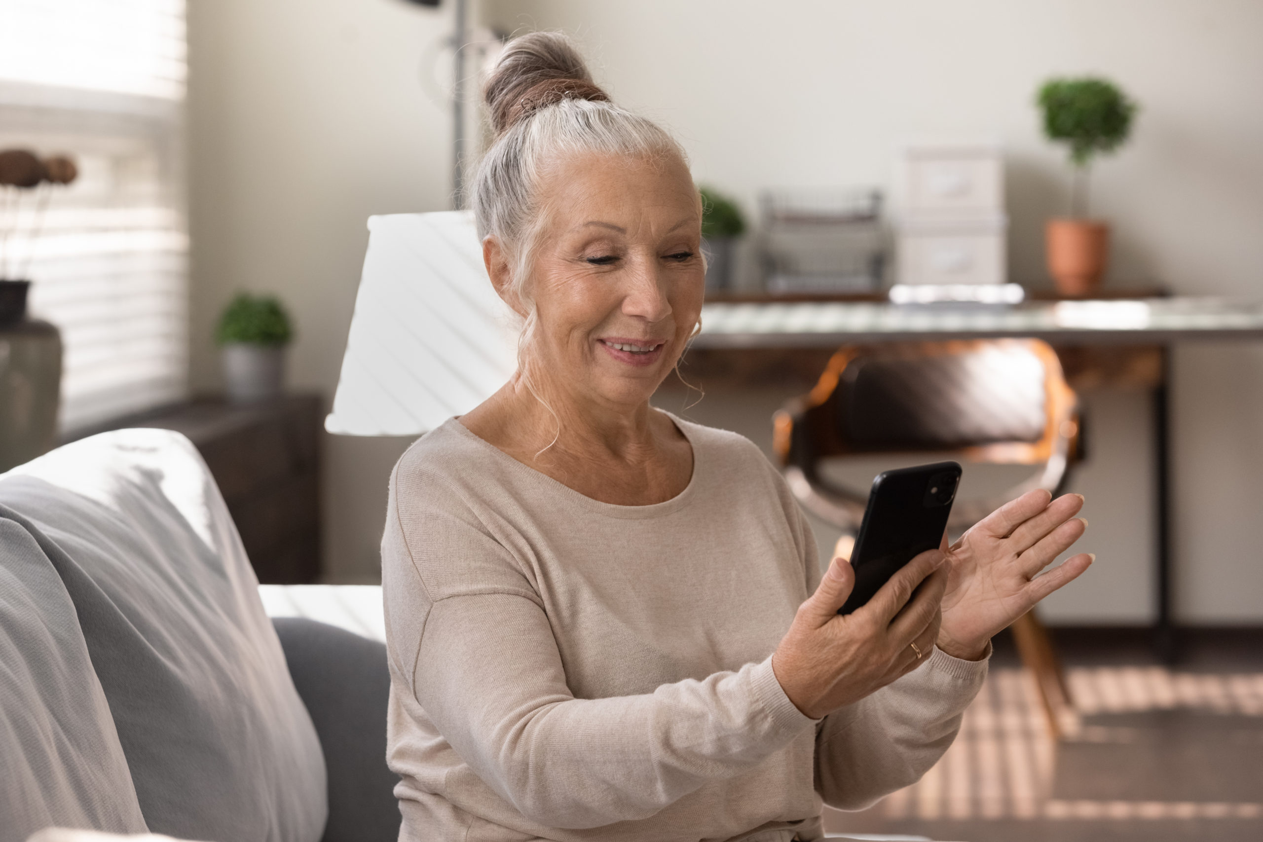 Happy elderly lady using smartphone at home, making video call