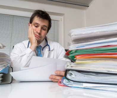 Bureaucracy in medicine concept. Tired overworked doctor is reading medical report. Many documents on desk.