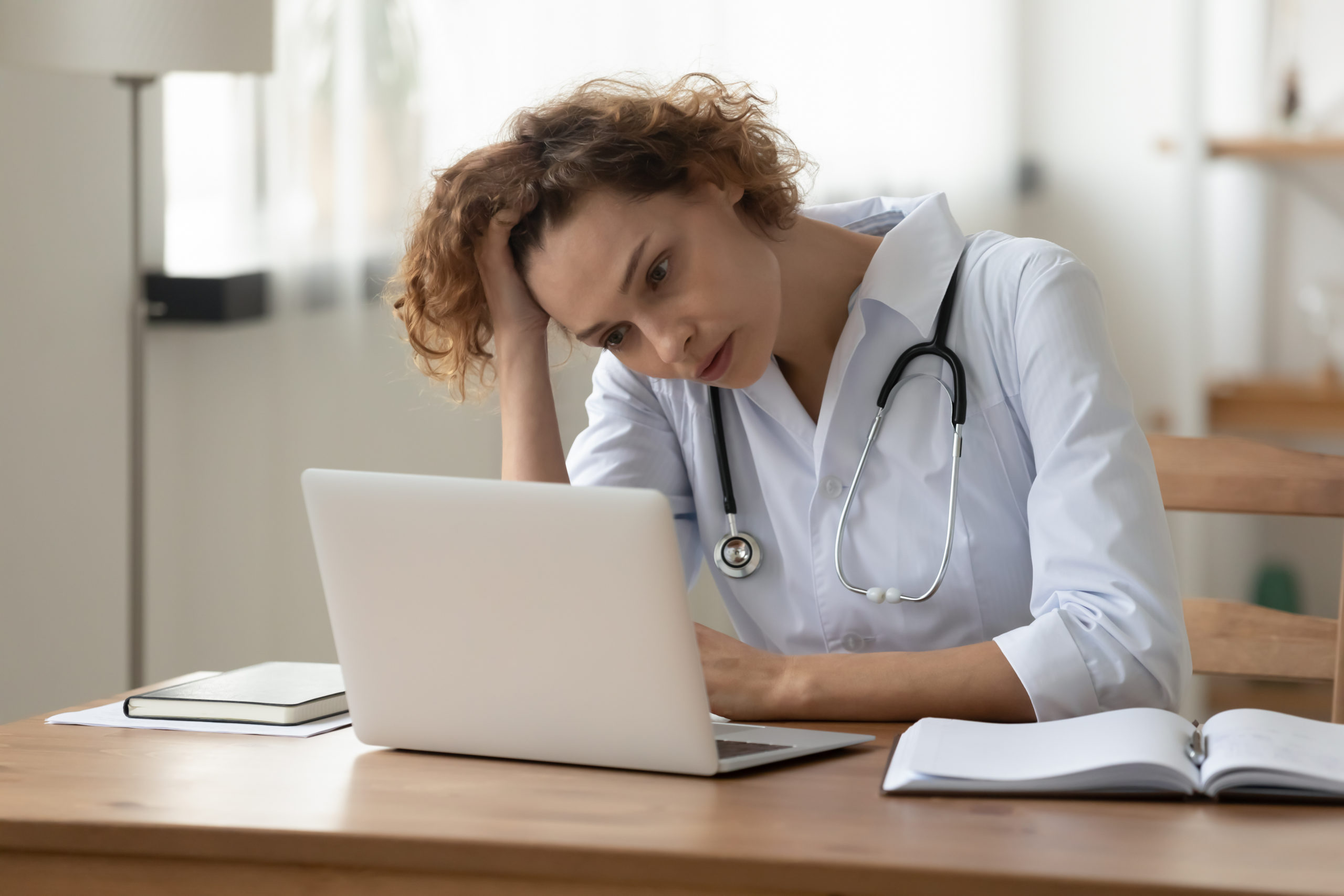 Stressed worried young female doctor looking at laptop at workplace
